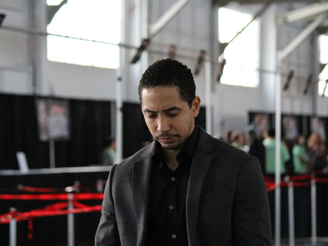 In this picture we can see man wore blazer. In the background we can see windows, wall, rod,...