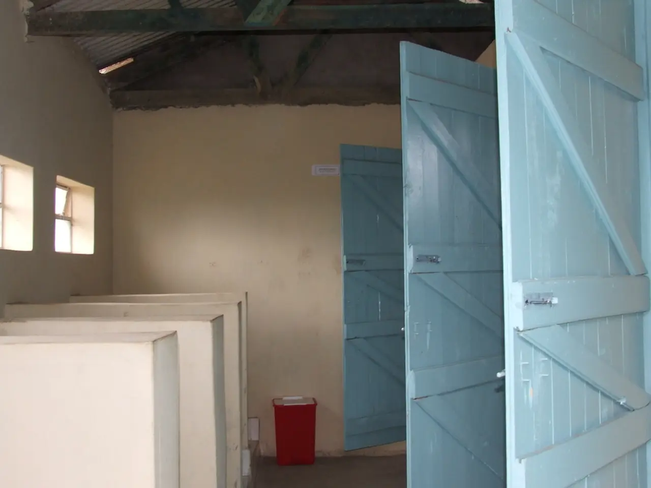 In this image we can see the blue color wooden doors, red color dustbin, ventilators, the wall and...