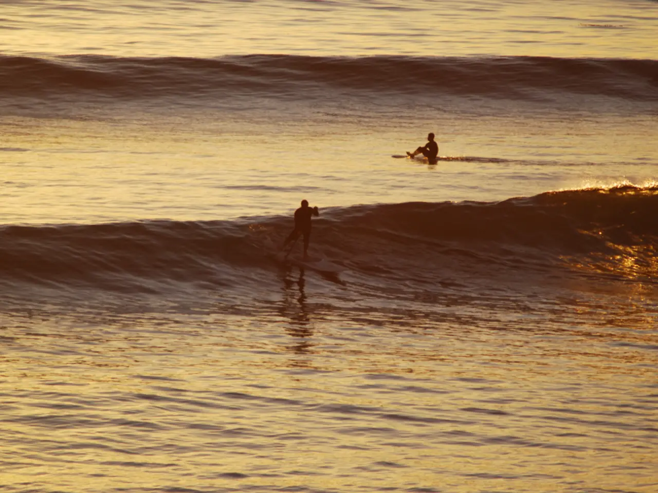 In this image we can see two persons in the water. Here we can see the waves.