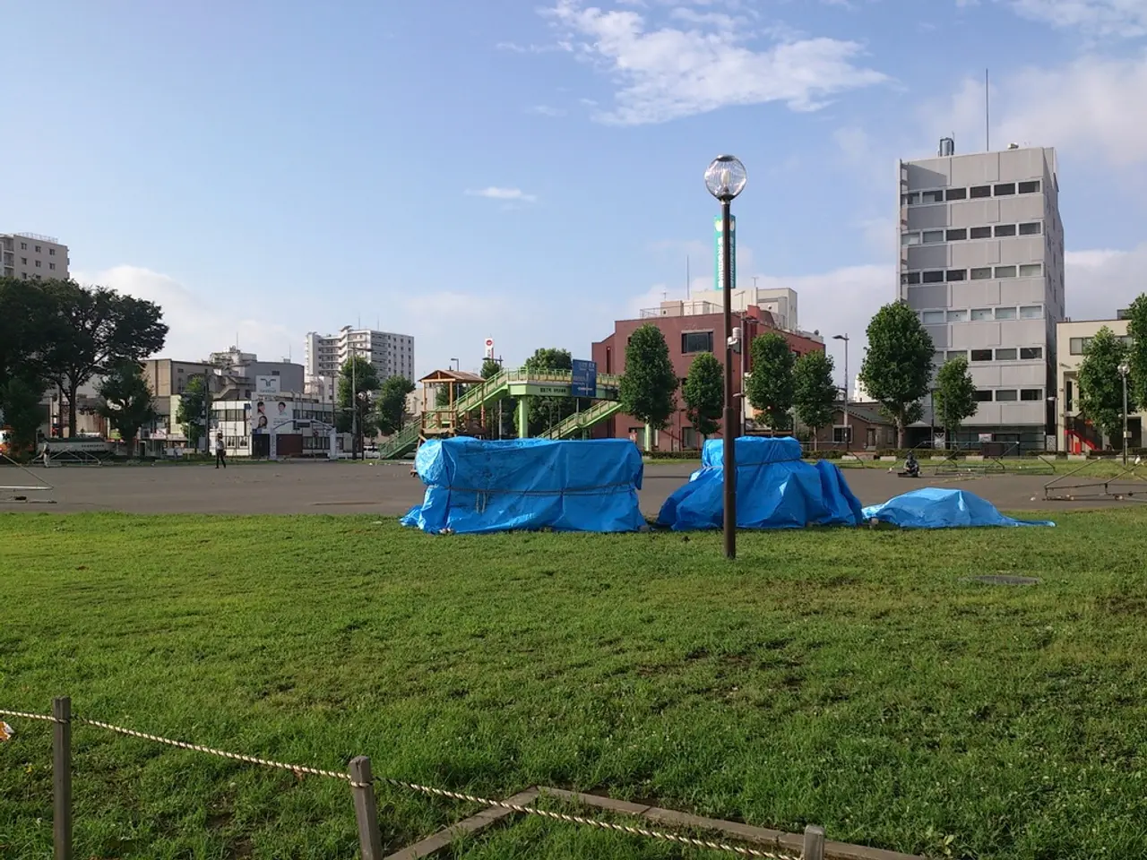 In this picture we can see there are poles, grass, rope and tarpaulin sheets. A person is walking...