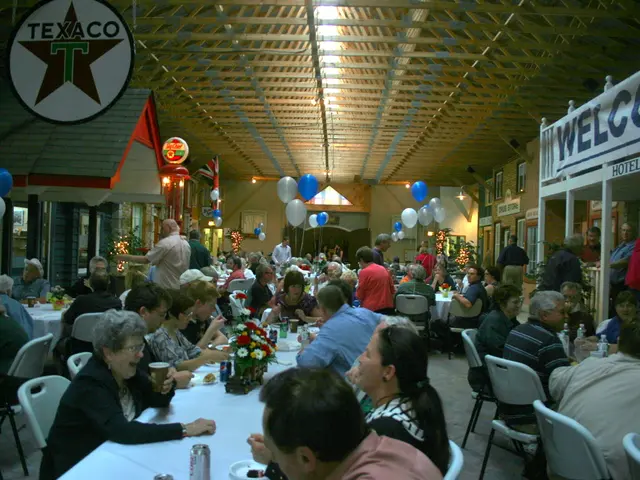 In this image we can see people sitting on the chairs and some are standing on the floor and tables...