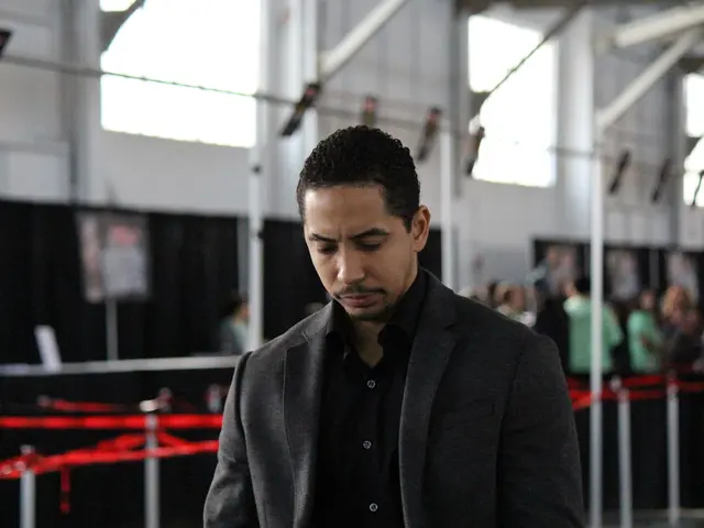 In this picture we can see man wore blazer. In the background we can see windows, wall, rod,...